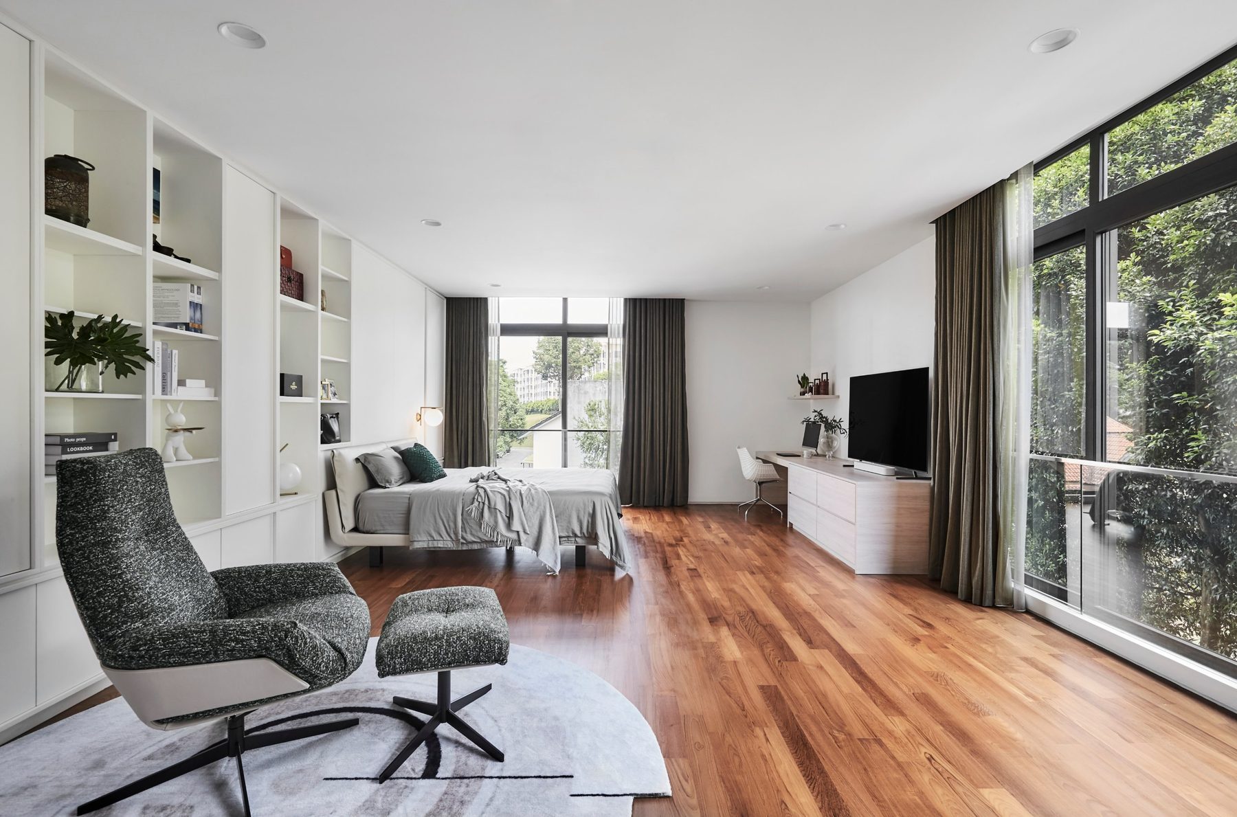 Spacious bedroom with built-in white shelving, a lounge chair and tall windows onto the greenery at the Namly Hill residence.